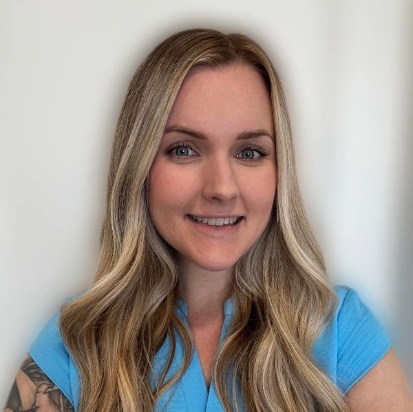 Smiling woman with long blonde hair and blue shirt against a light background.