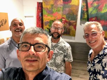 Four smiling men in an art gallery.
