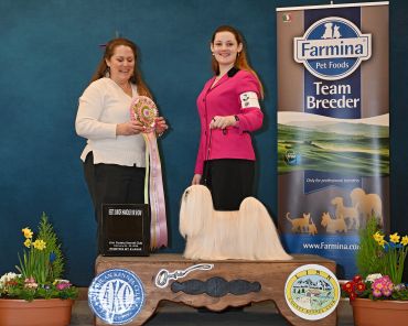 Two women with a long-haired dog at a dog show award ceremony.