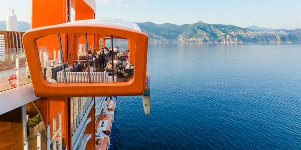 Orange observation pod on a cruise ship with sea and mountains.