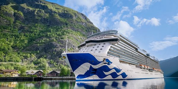 Large cruise ship in a scenic fjord with green mountains.