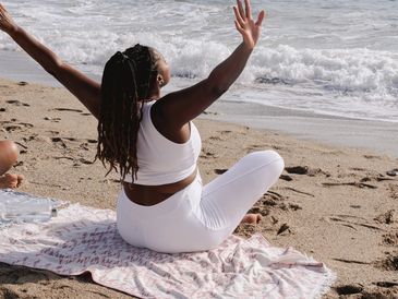 Woman practicing yoga on the beach with arms raised.
