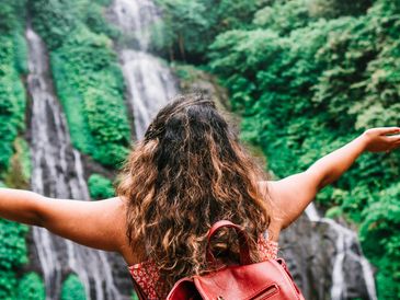 Person with arms open facing a waterfall.