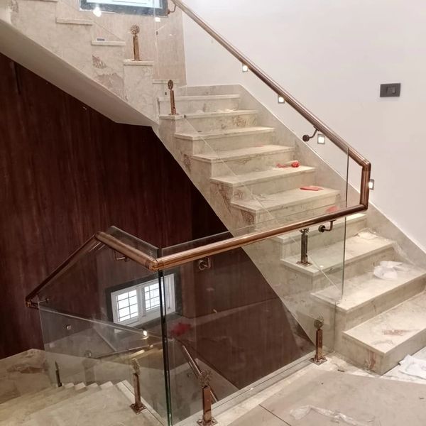 Modern marble staircase with glass and bronze railing in a well-lit interior.