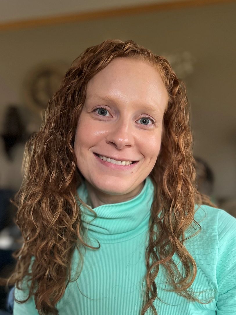 Smiling woman with curly red hair in a turquoise turtleneck.