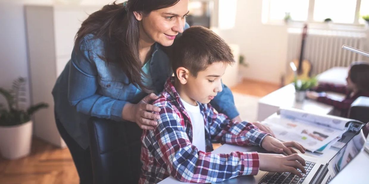 Woman helping boy with laptop at home.