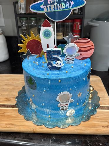 Blue space-themed birthday cake with rockets, astronauts, and planets.