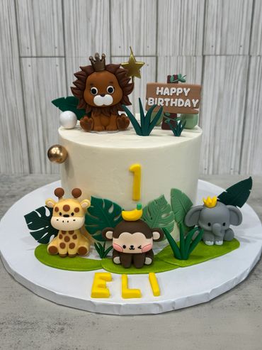 A jungle-themed birthday cake with cute animal figures and a number 1 topper.