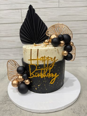 Elegant black and gold birthday cake with decorative balls and fans.