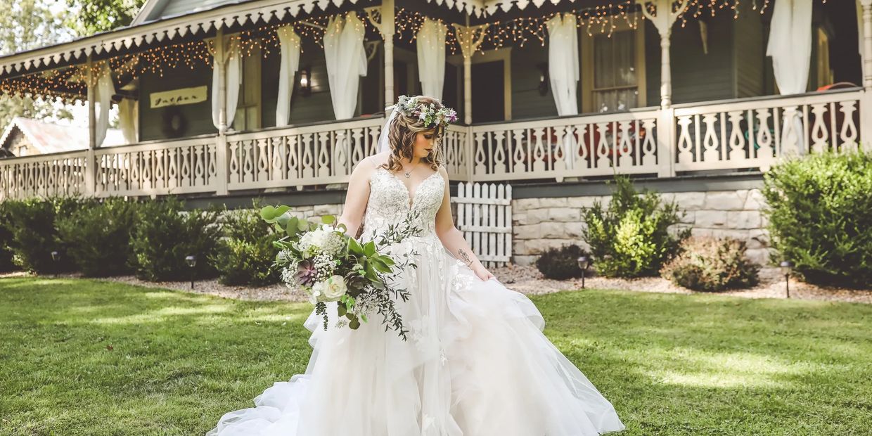 Bride in wedding dress holding bouquet of flowers in front of rustic house with wrap around porch