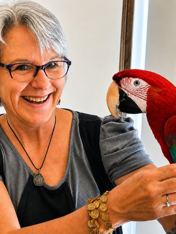 Smiling woman holding a colorful parrot.