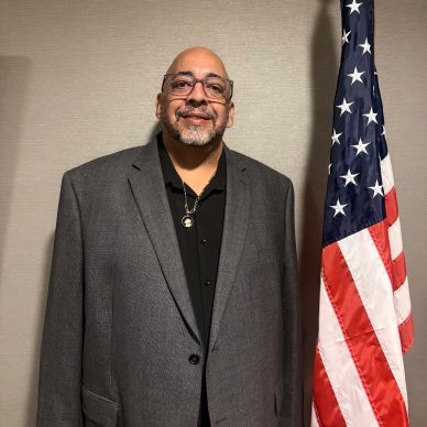 Man in gray suit standing next to the American flag.
