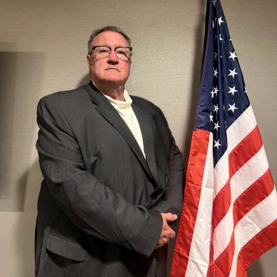 Man in suit standing next to American flag.