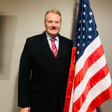 Man in suit posing next to American flag.