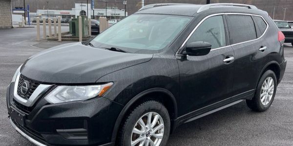 Black Nissan SUV parked on wet asphalt in a dealership lot.