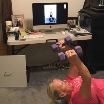 Woman lifting dumbbells while following an online workout on her computer.