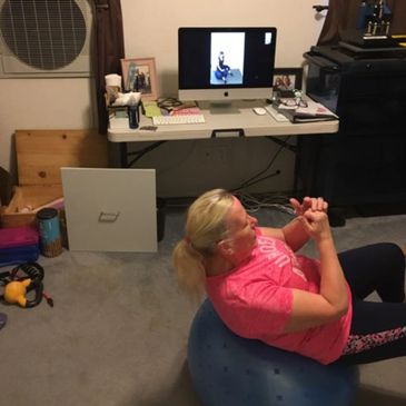 Woman exercising on a stability ball following a workout video on a computer.
