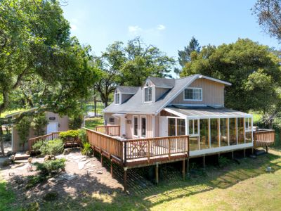 Cozy countryside house with a spacious wooden deck and sunroom surrounded by trees.
