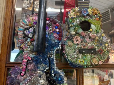 Two guitars decorated with colorful beads, jewels, and ornaments hanging on a wall.