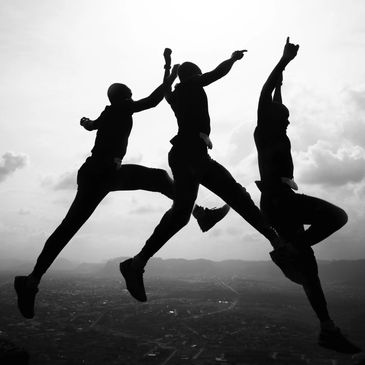 Silhouettes of three people jumping against a cloudy sky.