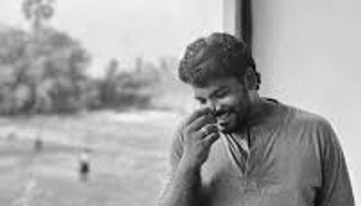 Man smiling and holding a plant near his face by a window.