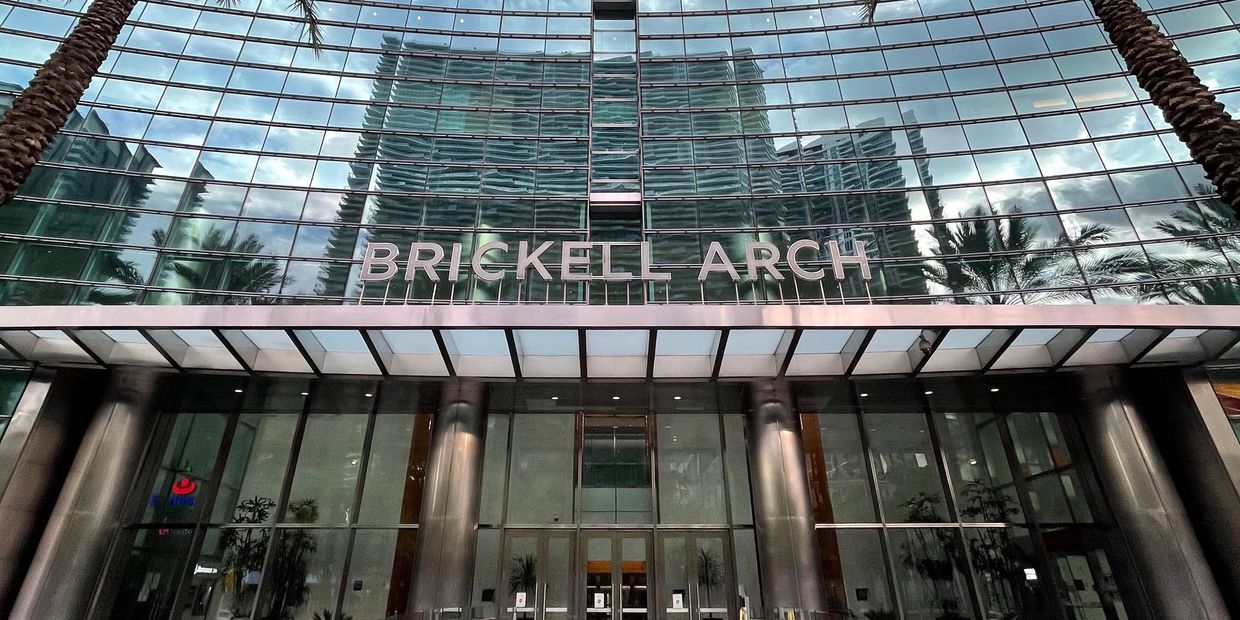 Facade of the Brickell Arch building with reflective glass and palm trees.