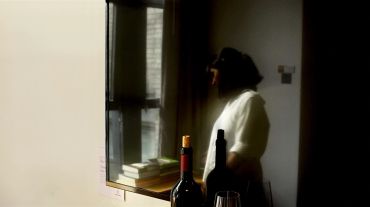 Woman looking out a window with wine bottles on the table.
