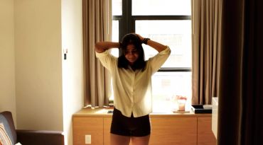 Woman standing with hands on head in front of window.