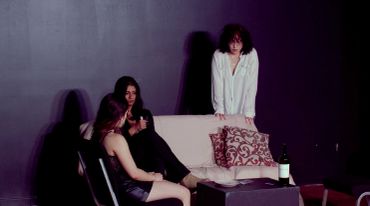 Three people in a dark room with a bottle of wine.