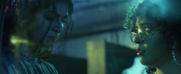 Two people in a dimly lit setting with intense looks.