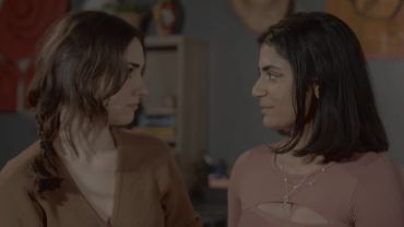 Two women looking at each other with smiles indoors.