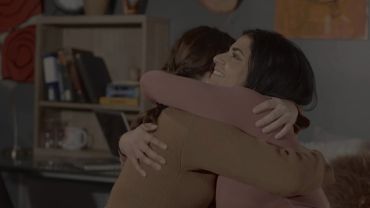 Two women warmly hugging each other indoors.