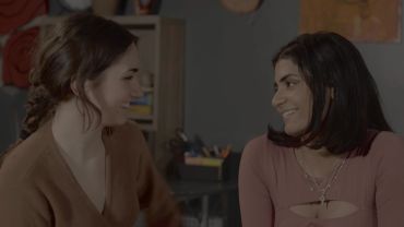 Two women smiling at each other in a cozy setting.