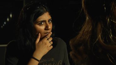 A woman looks thoughtfully while covering her mouth with her hand.