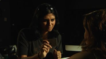 Two women engaged in a close conversation in dim lighting.