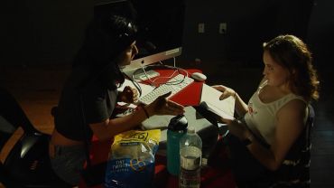 Two women working together at a dimly lit desk.