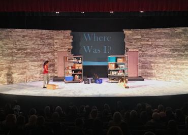 Theater stage with two women and shelves in front of a question display.