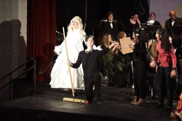 A stage performance with a person in a white costume and others interacting.