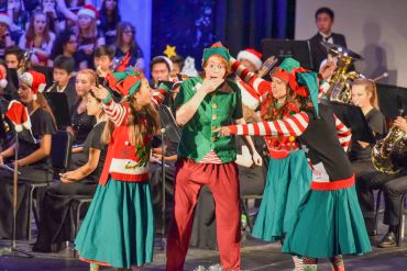 People dressed as elves performing on stage with a band in the background.