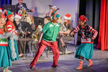 People in Christmas costumes dancing on stage with a band.
