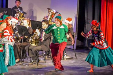 Elf and festive characters performing with band in holiday concert.