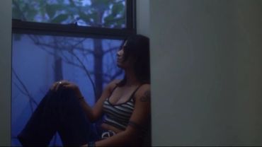 Woman sitting by a window in dim light, lost in thought.