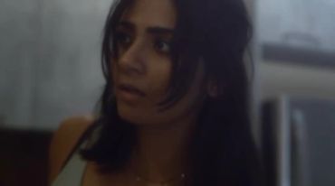 A woman looks thoughtfully to the side indoors.