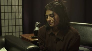 A woman sits pensively in a dimly lit room.