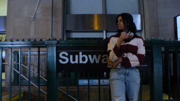 Woman standing near a subway entrance at night.