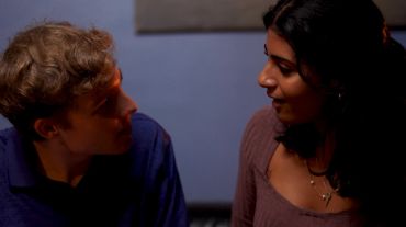 A man and woman engaged in conversation in dim lighting.