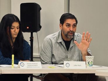 Two individuals seated at a panel table during a discussion or meeting.