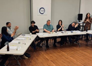 People sitting around a table clapping in a meeting room with TDB logo.