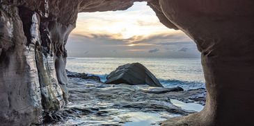 View of the ocean and sunset from inside a rocky cave.