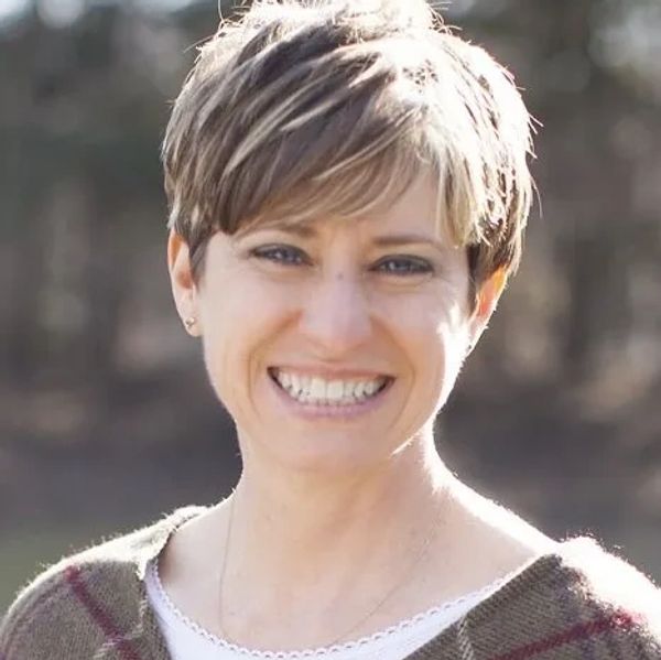 Smiling woman with short hair outdoors on a sunny day.